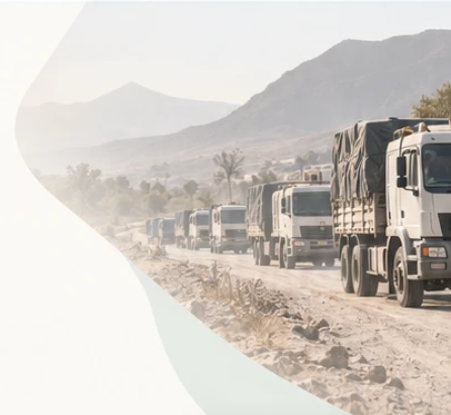 A convoy of aid trucks on a dusty road below mountains